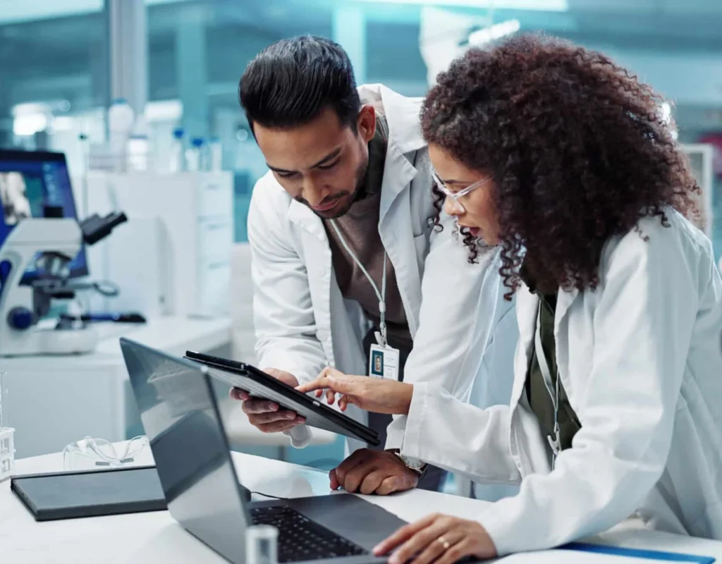 Healthcare professionals reviewing operational data on tablet and laptop in a clinical lab